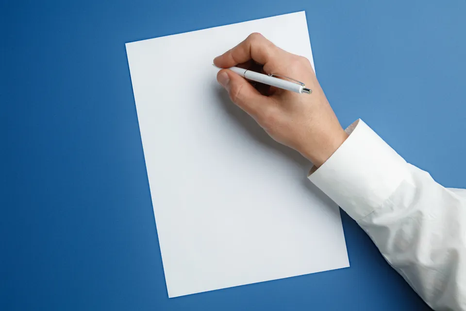 Hand mit Stift beim Schreiben auf einem leeren Blatt vor blauem Hintergrund