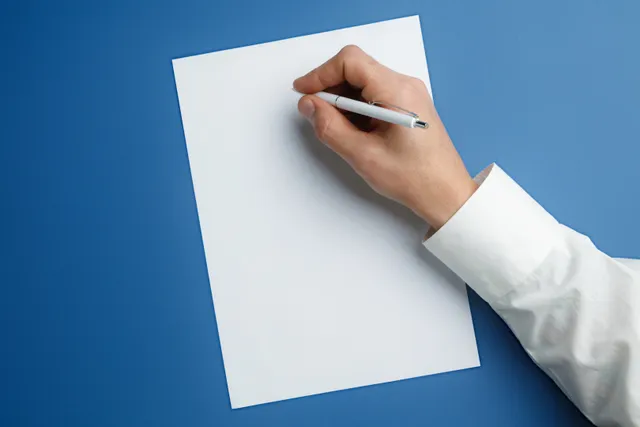 Hand mit Stift beim Schreiben auf einem leeren Blatt vor blauem Hintergrund